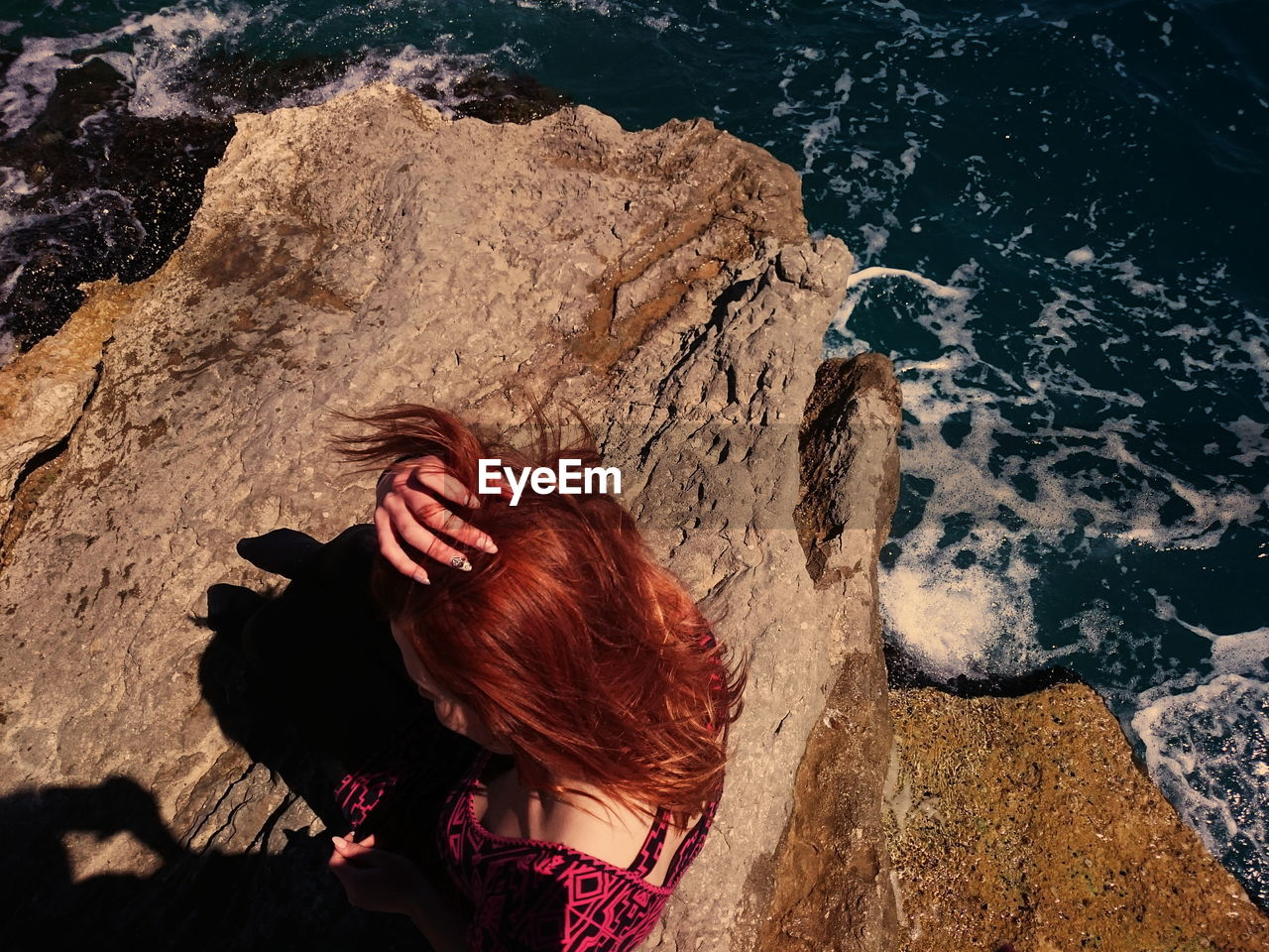 Redhead woman sitting on rock at beach