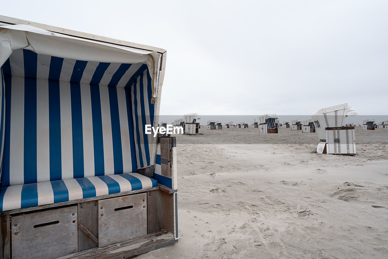 Hooded beach chairs on sand against clear sky