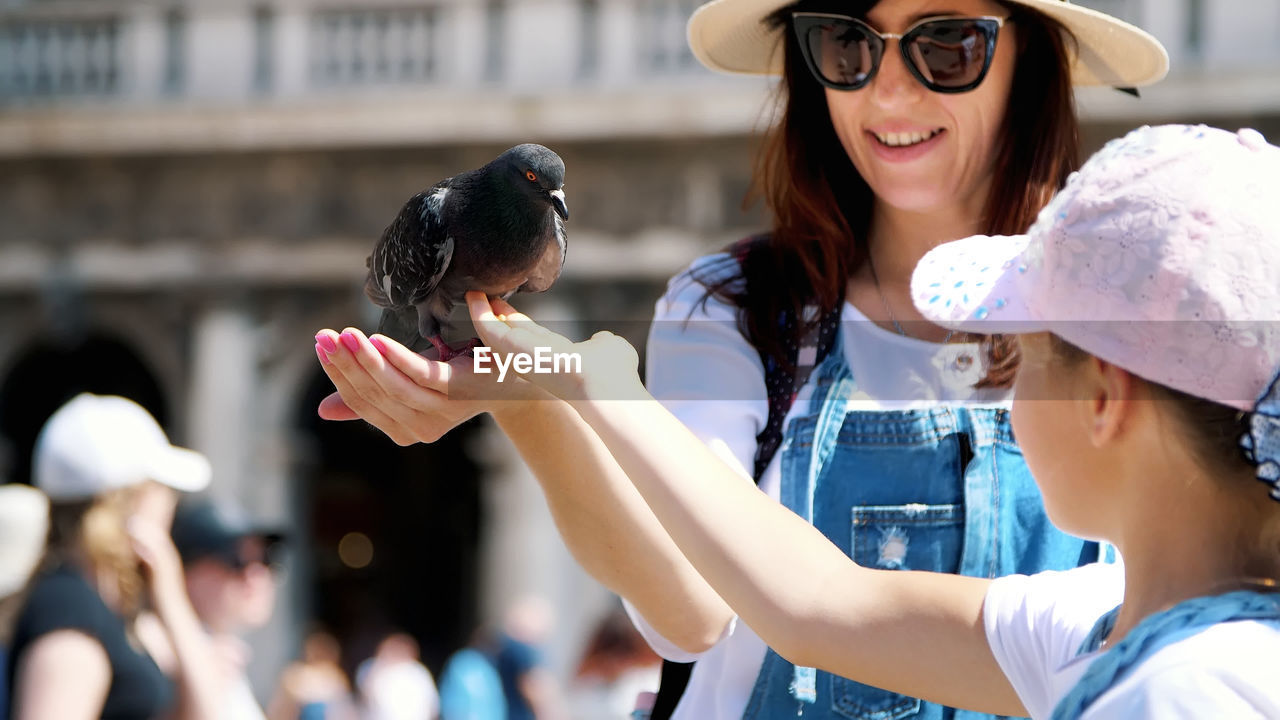 View of happy woman and kid girl, tourists, holding pigeons, feeding, play with them