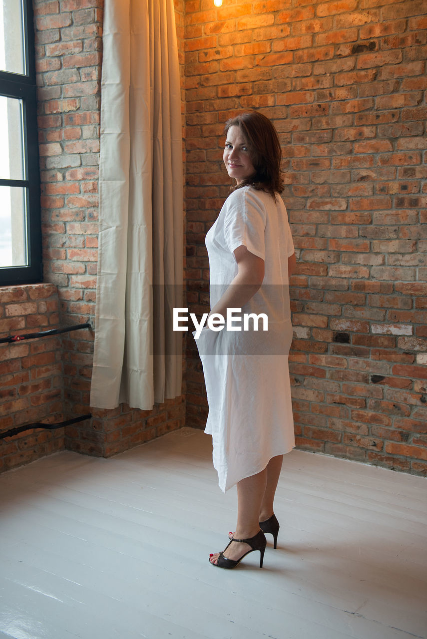 Full length portrait of woman standing against brick wall