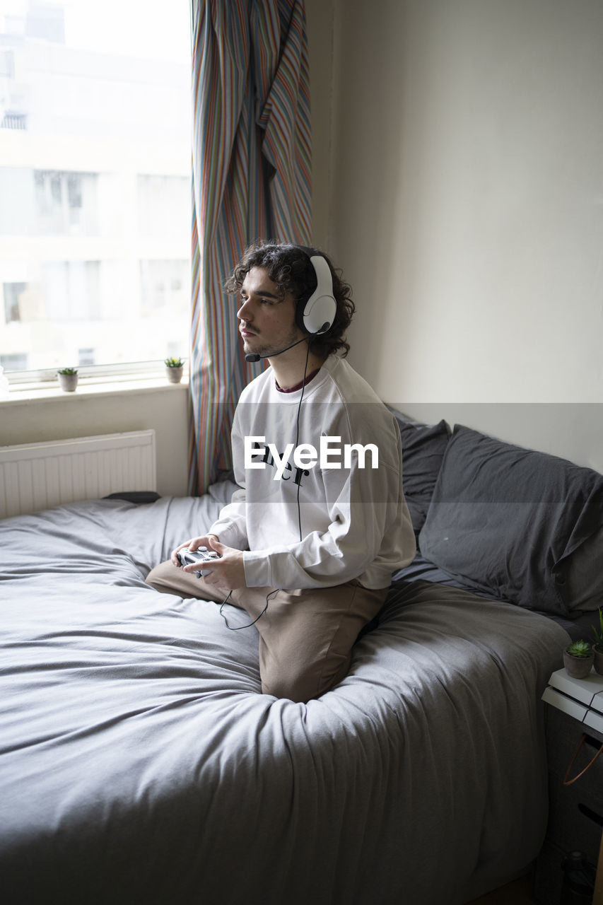 Man kneeling while playing video game on bed at home