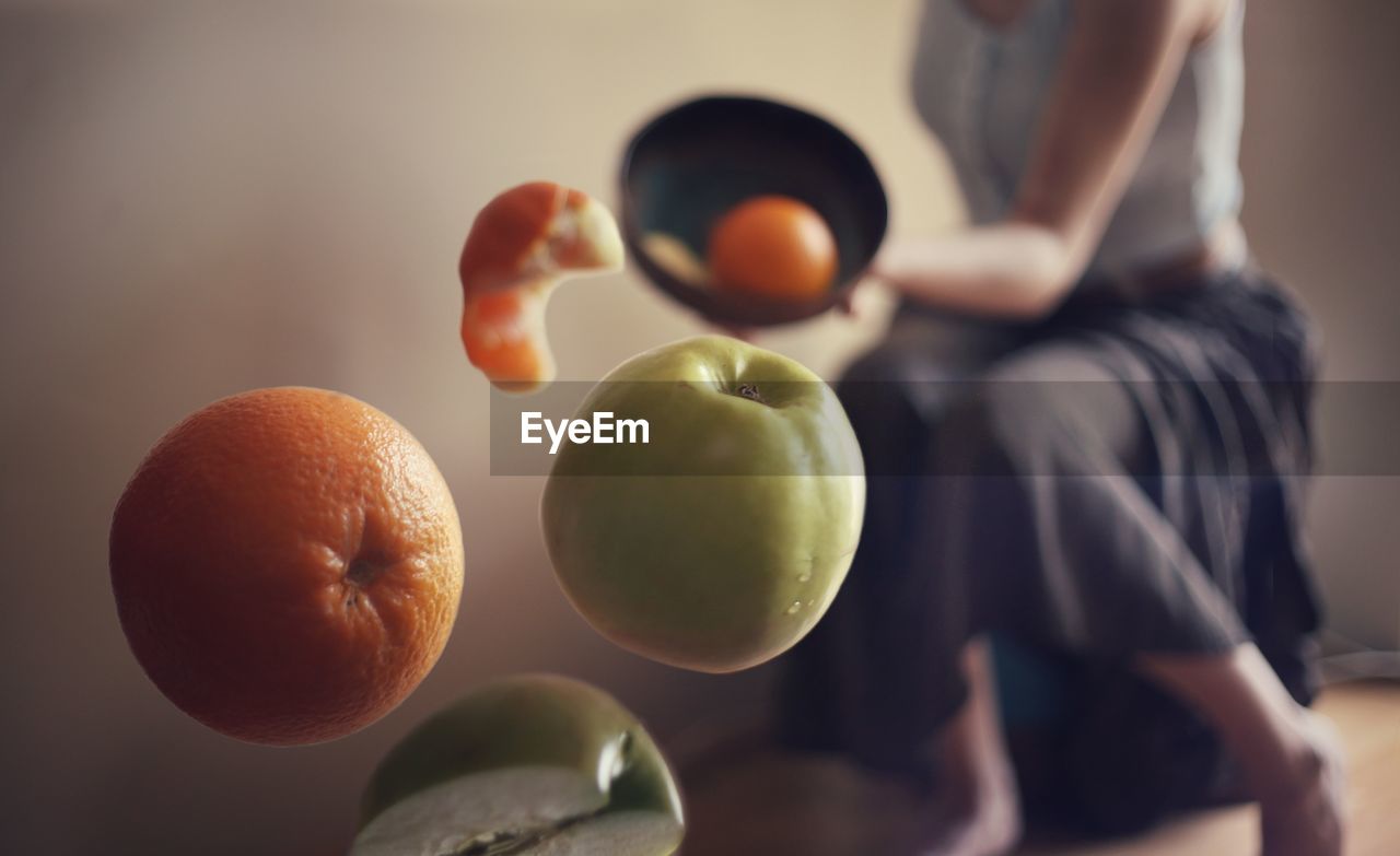 Midsection of woman throwing fruits in bowl at home