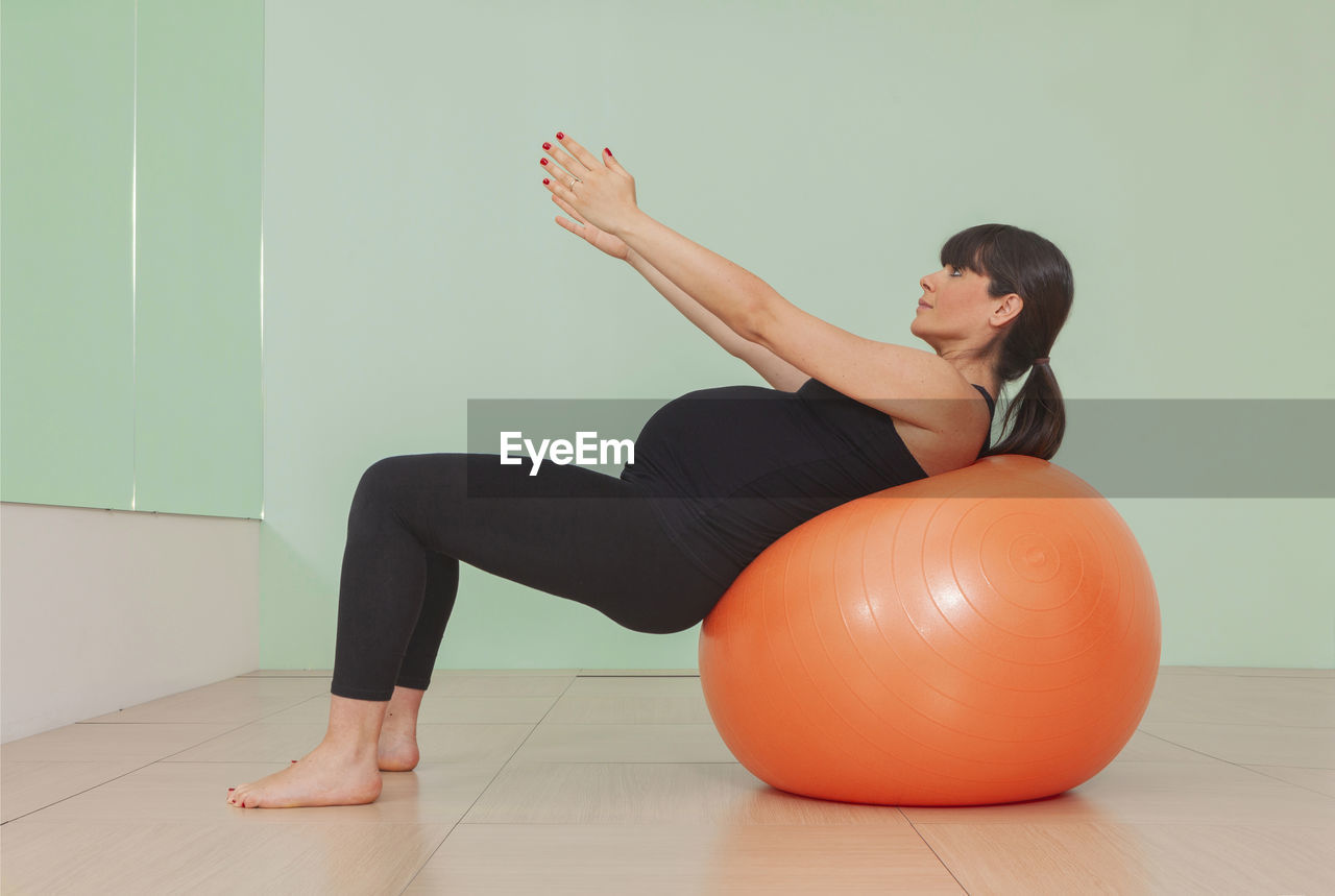 Full length of pregnant woman exercising with fitness ball in gym