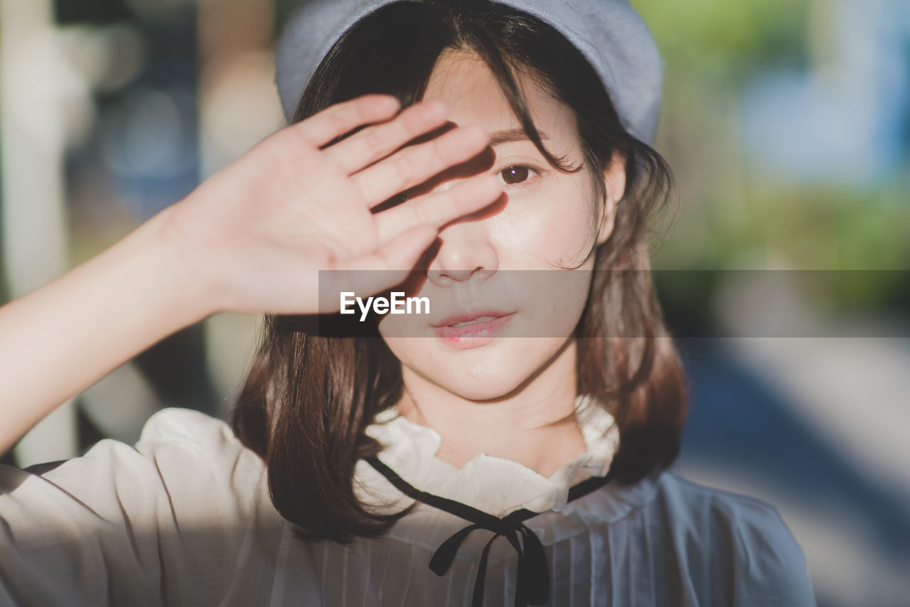 Close-up portrait of young woman shielding eyes on sunny day