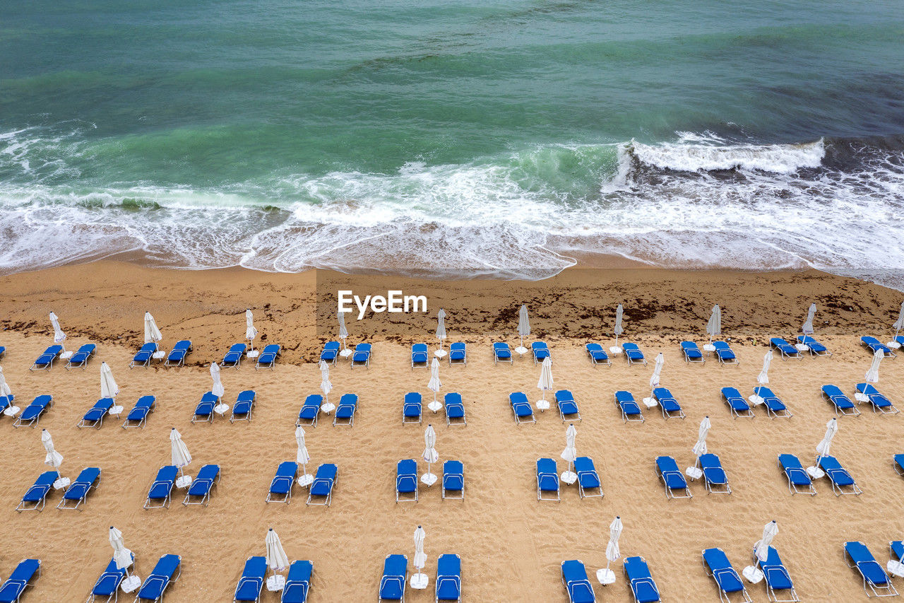 Aerial view of a fantastic beach with, blue lounge chairs, umbrellas, and turquoise sea.