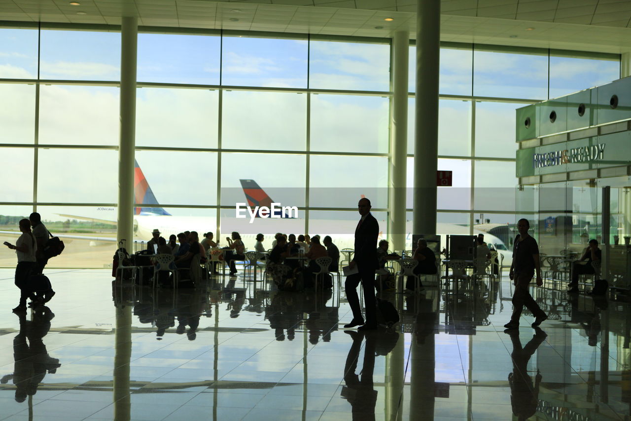 group of people, reflection, airport, window, transportation, large group of people, travel, airport departure area, crowd, silhouette, air vehicle, glass, mode of transportation, indoors, government, architecture, men, airplane, adult, building, airport terminal, journey, passenger, women, military, day, city, business, walking, nature, person