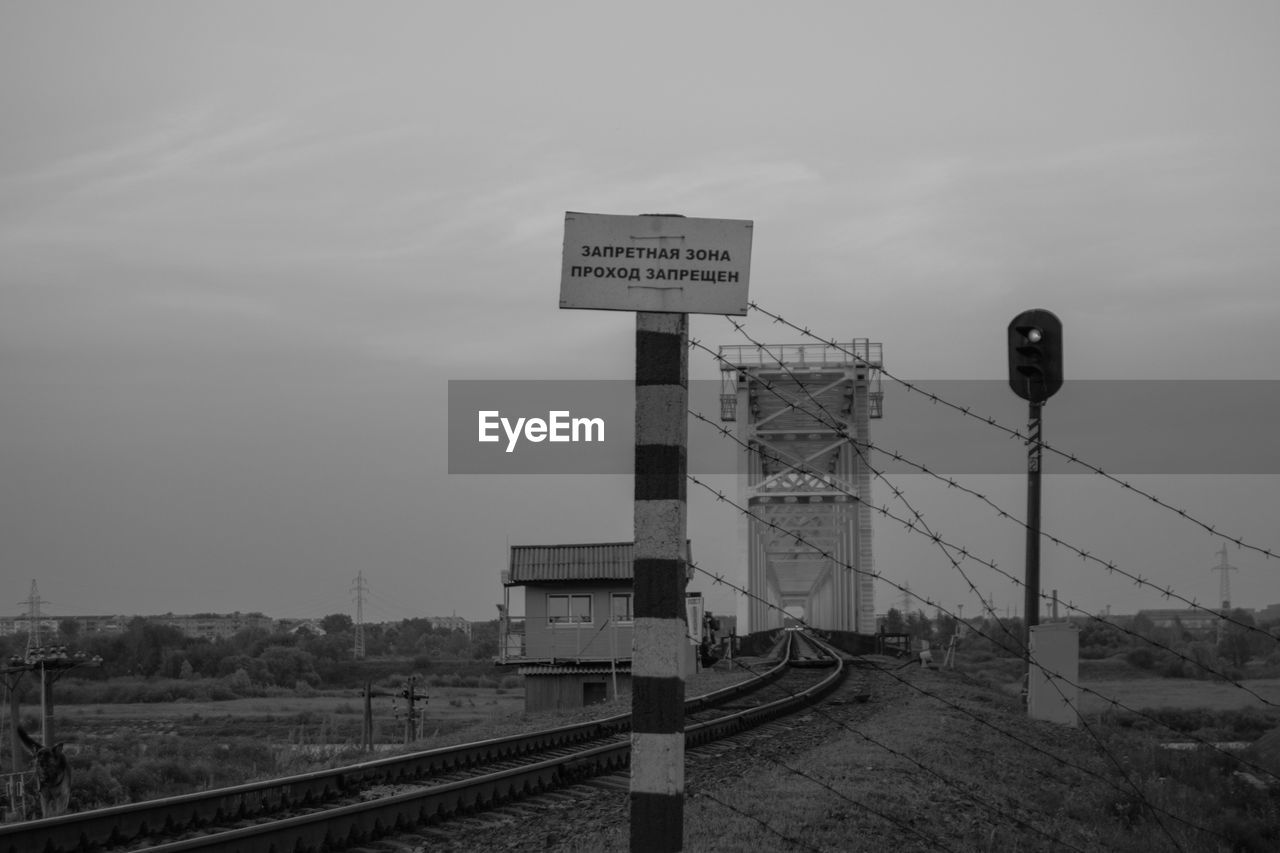 Road sign by railroad tracks against sky