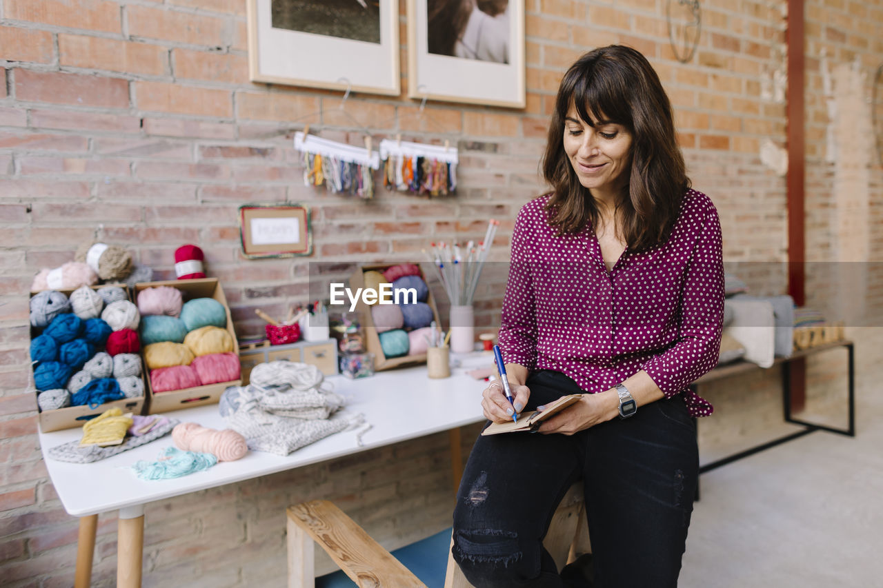 Smiling woman in knitting studio taking notes