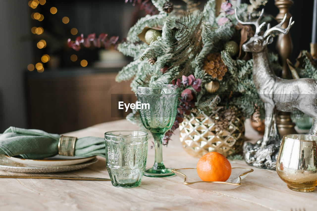 Festive christmas dinner setting. green wine glasses, branches of fir or spruce in a vase, plates