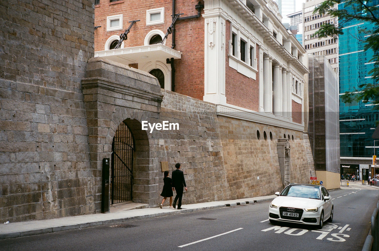 REAR VIEW OF PEOPLE WALKING ON STREET BY BUILDINGS