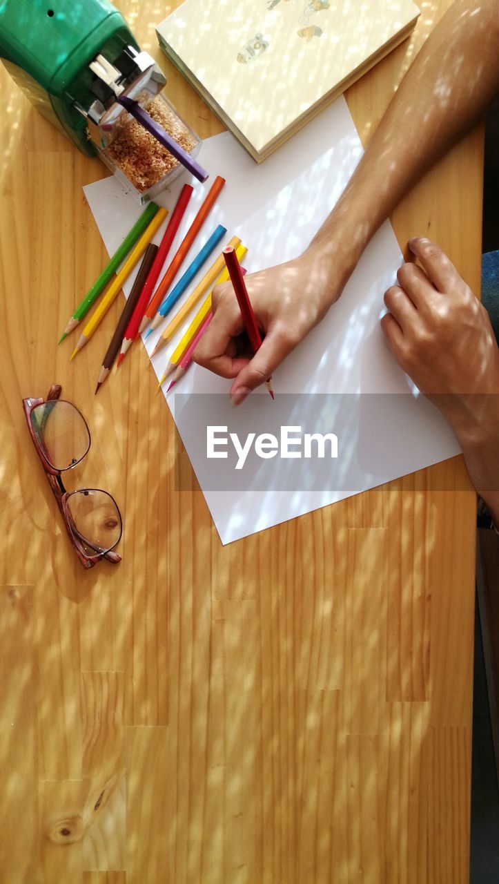 Cropped image of woman holding colored pencil on paper at table