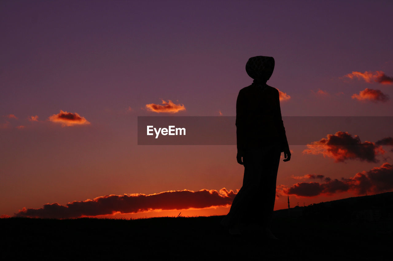 Silhouette woman standing on land against sky during sunset