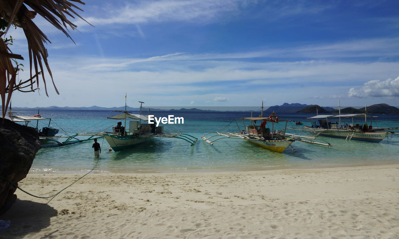 Outrigger fishing boats moored at sea shore against sky