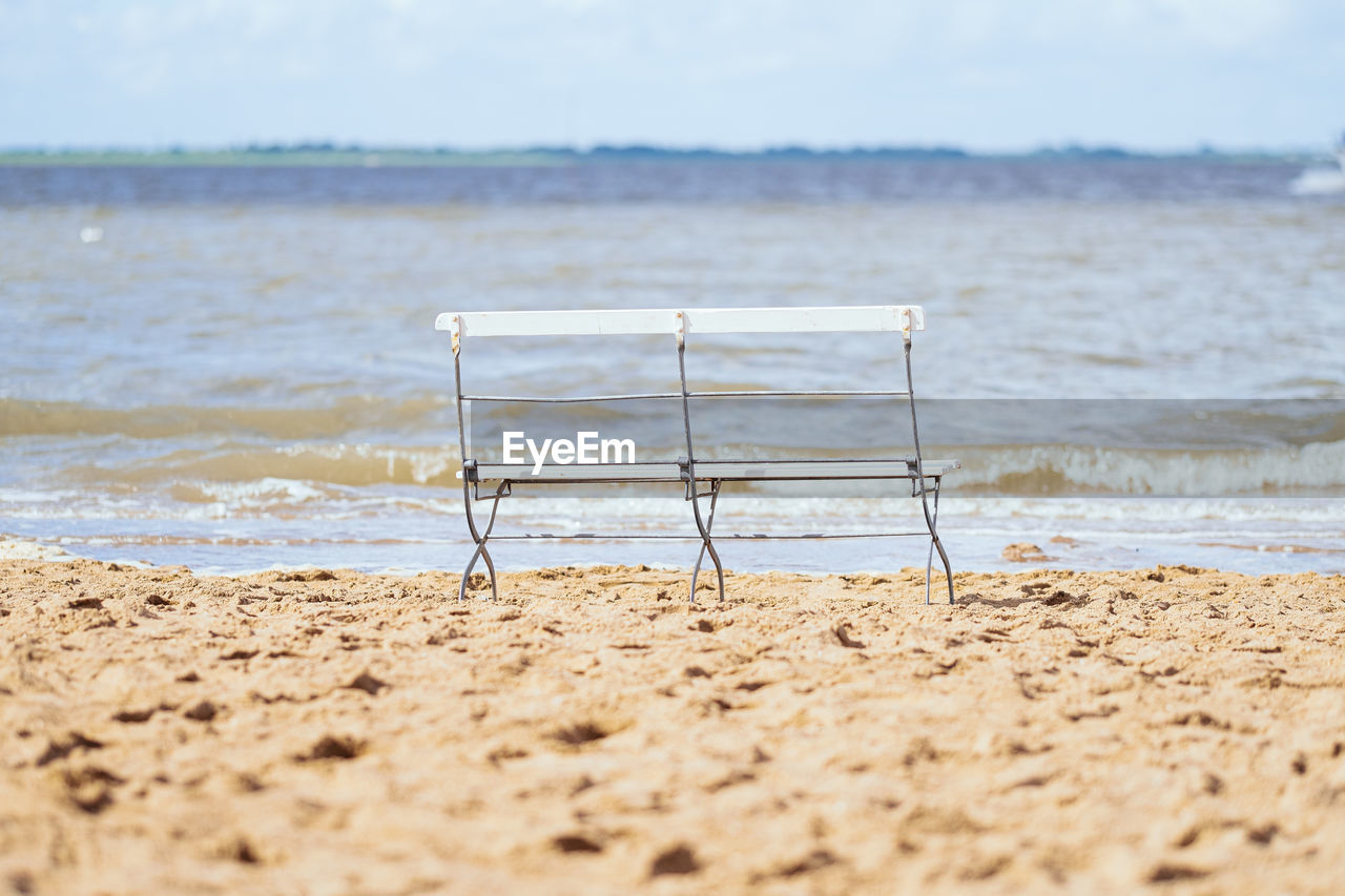 Garden bench on beach against sky