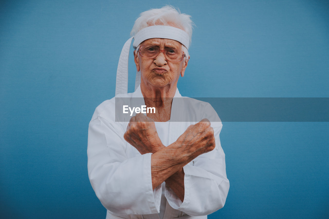 Portrait of senior woman doing karate against blue background