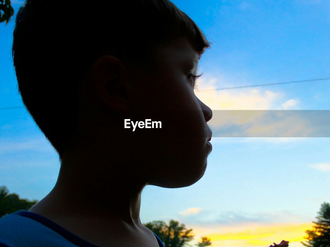 Close-up of boy looking away against sky during sunset