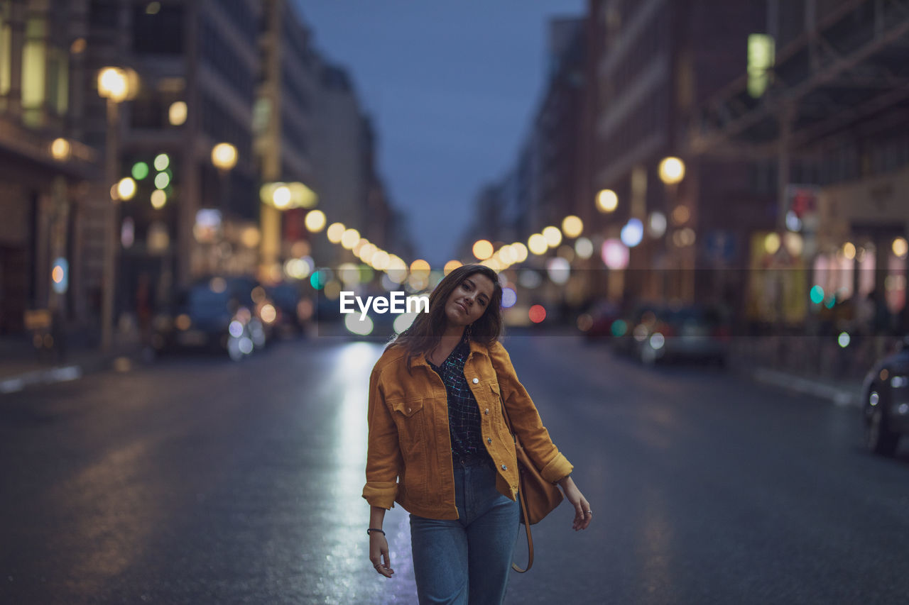 Portrait of young woman standing on road in city at night