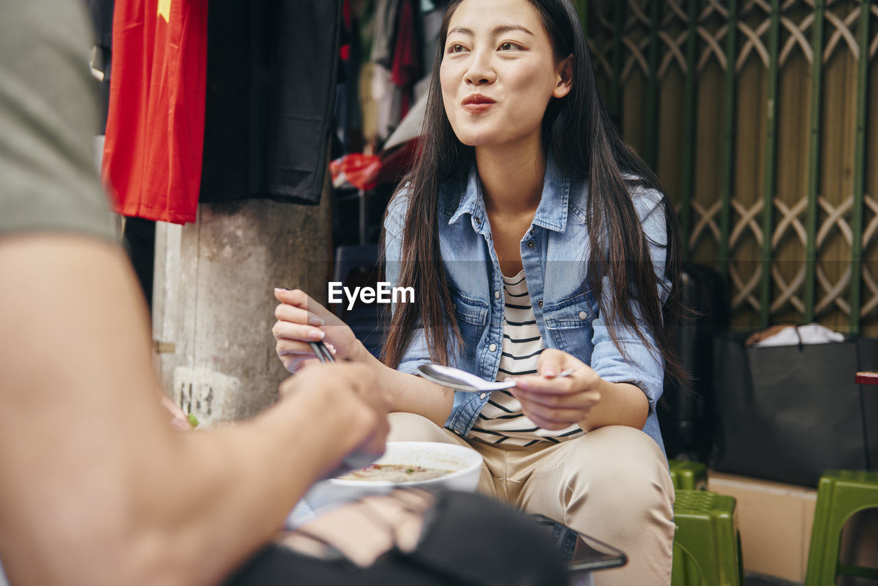 Smiling woman eating food while sitting outdoors