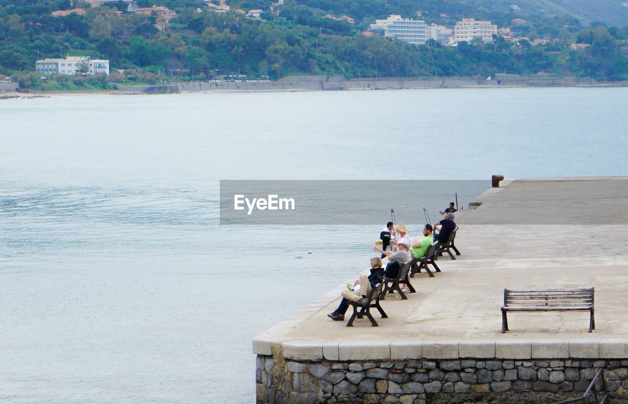 High angle view of people sitting on benches at pier in sea