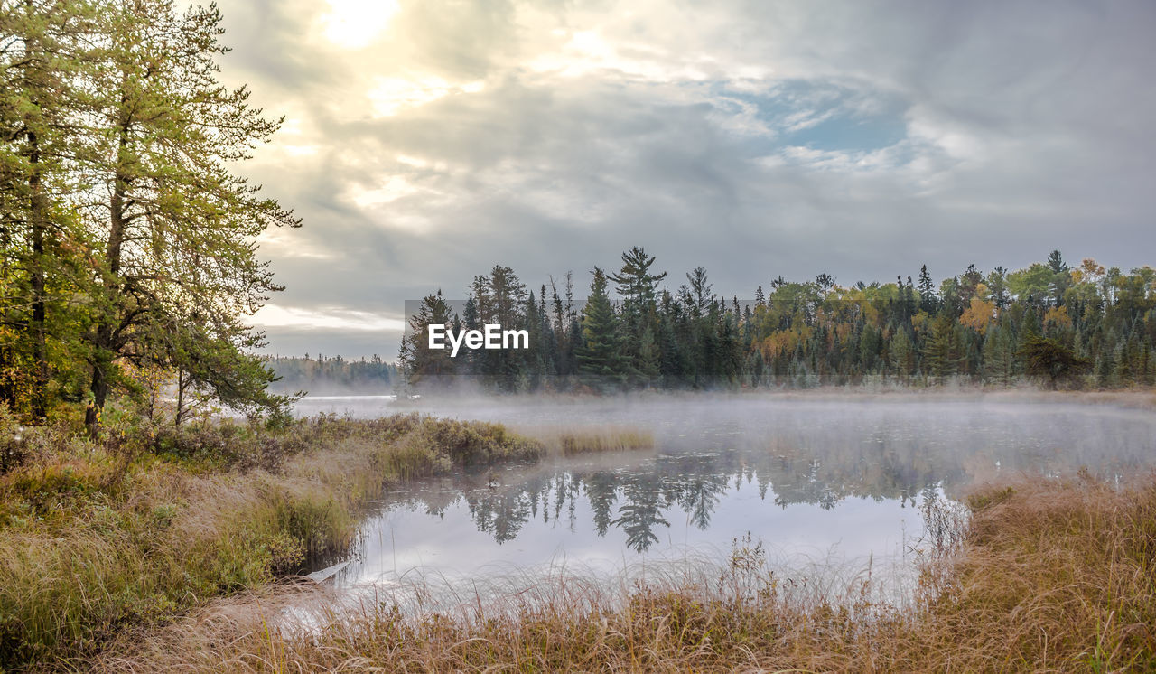 Scenic view of calm lake against cloudy sky during foggy weather