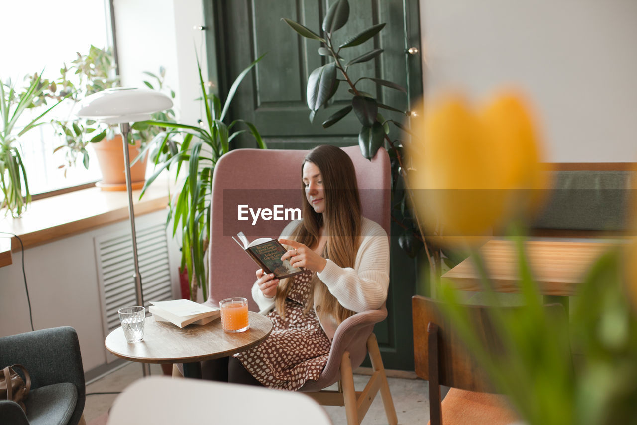 Millennial woman reading a book sitting in chair in cafe.candid lifestyle in cafe with cozy interior