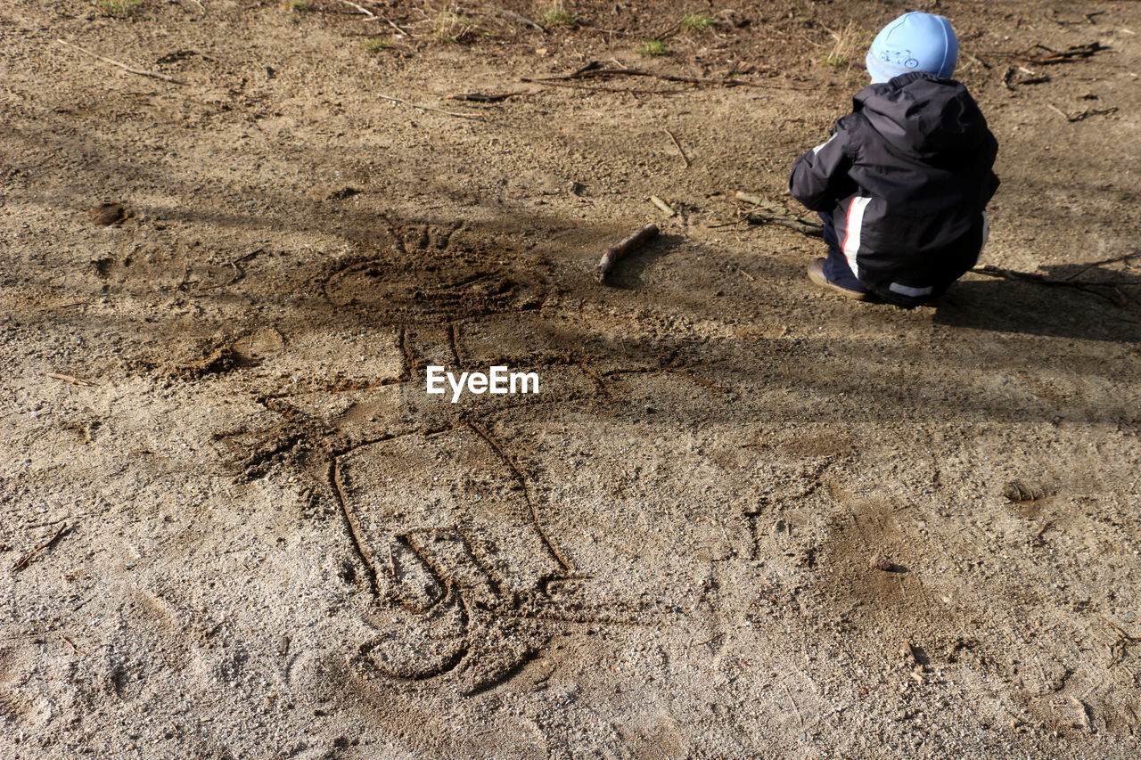 Rear view of child crouching on dirt road