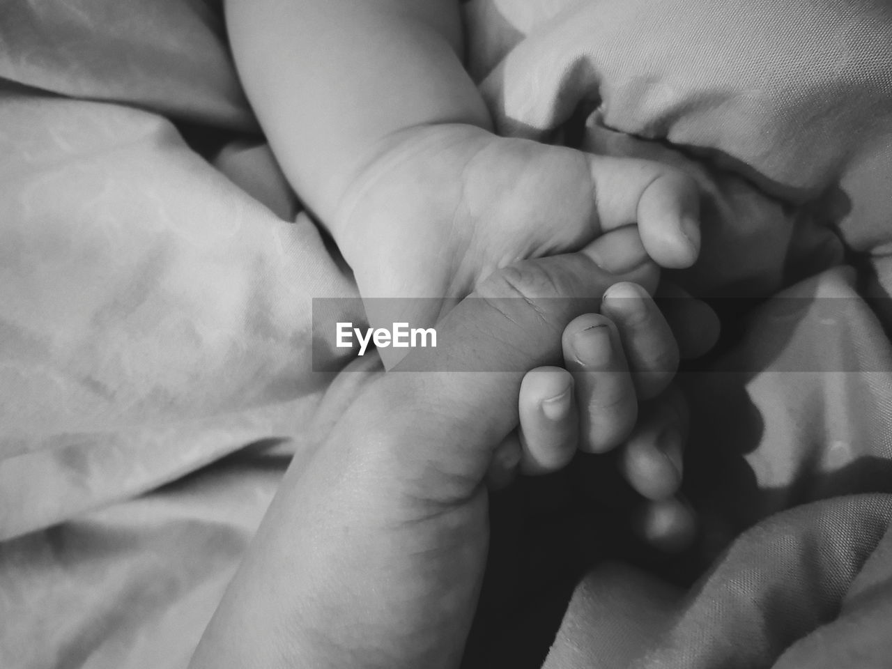 Close-up of baby hands on bed holding mom's hand