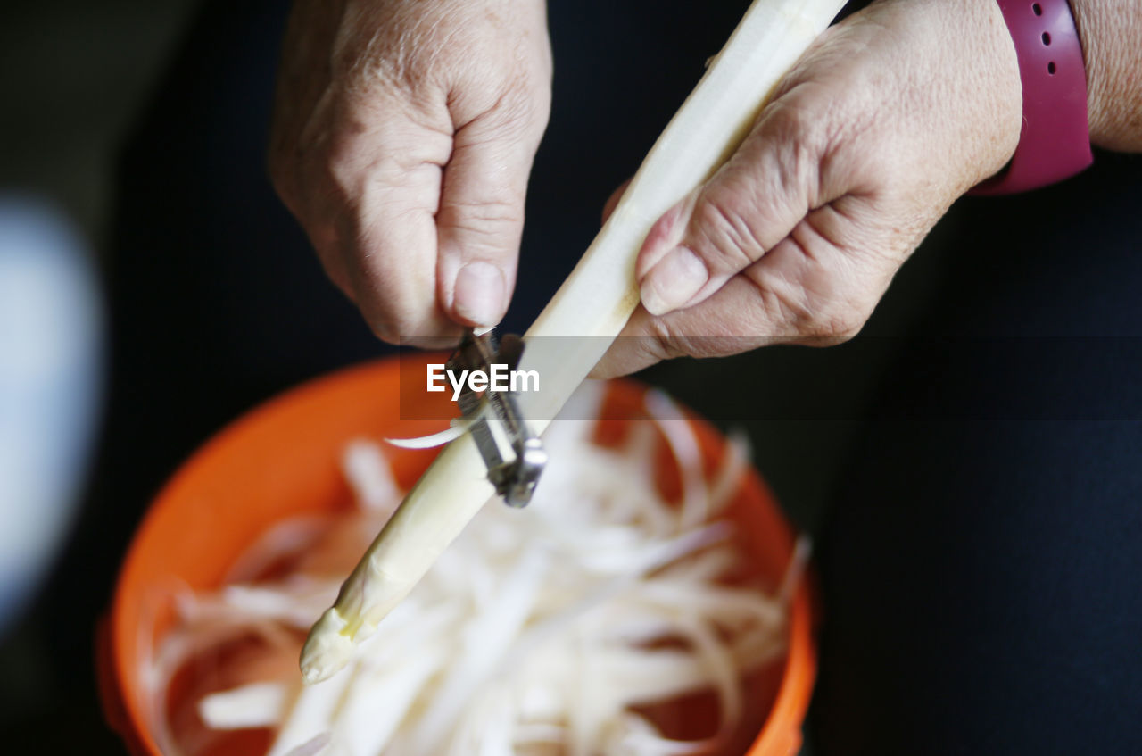 Cropped hands of woman peeling off asparagus in kitchen