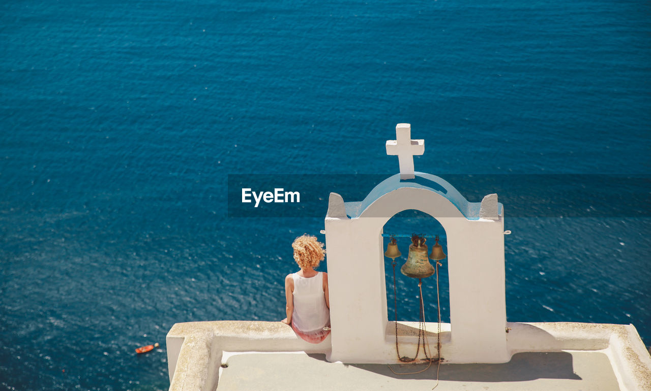 Rear view of woman sitting on chapel against sky