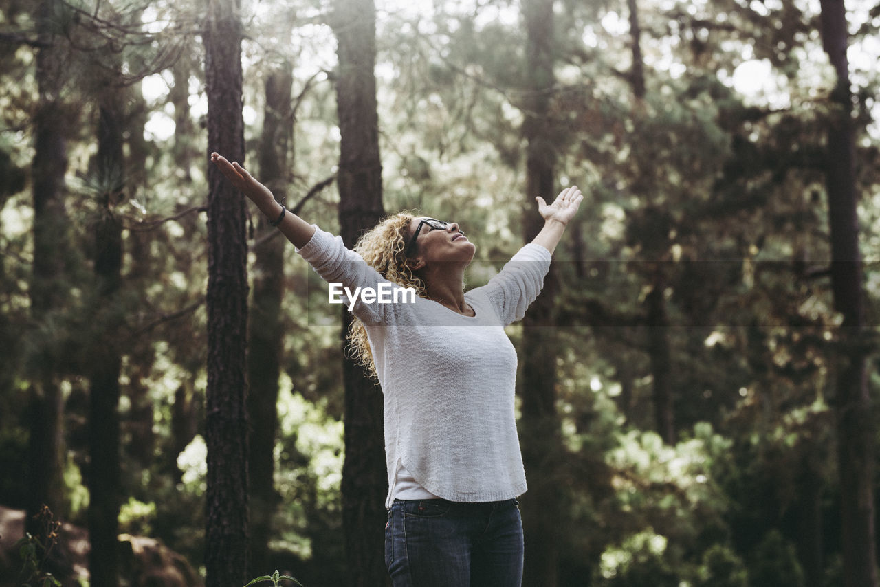 Beautiful woman with arms raised standing in forest