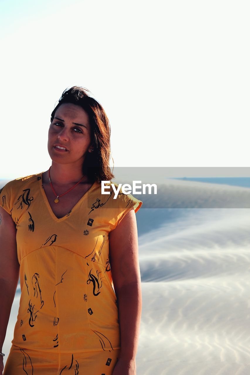 Portrait of young woman standing at beach against clear sky