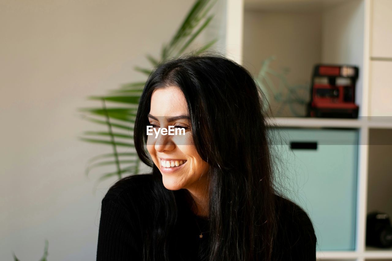 Close-up of smiling young woman looking away while sitting at home