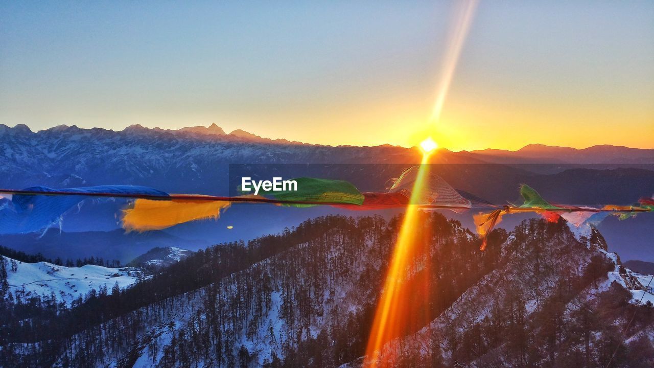 Colorful prayer flags waving against snowcapped mountains during sunset