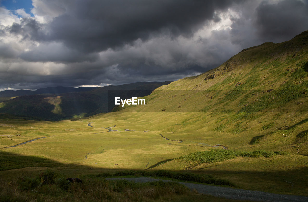 Scenic view of green mountains against cloudy sky