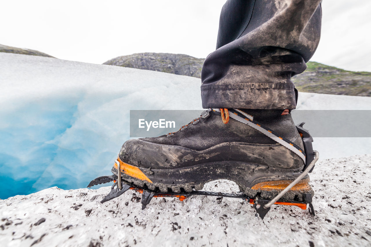 Close up of a hiking shoe on ice covered rock against sky