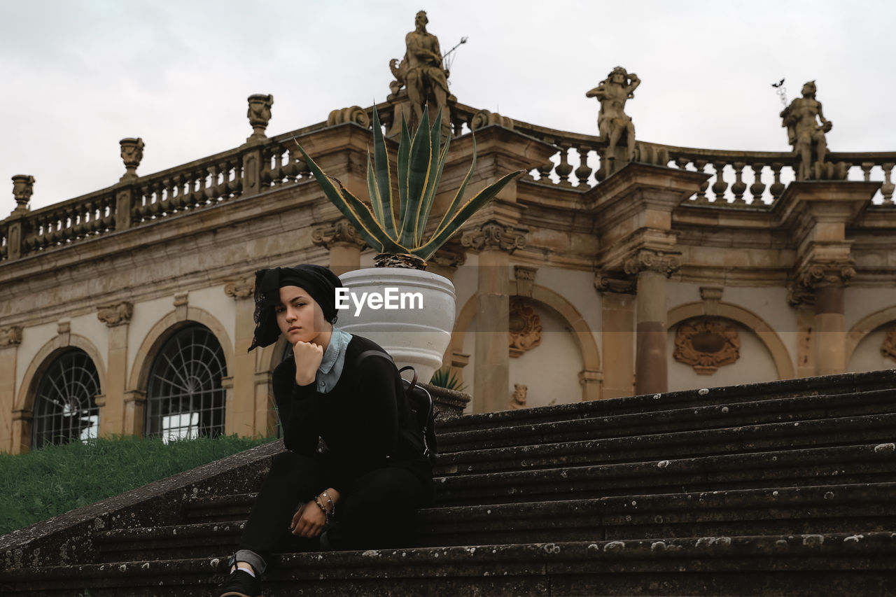 Portrait of woman sitting on staircase against sky