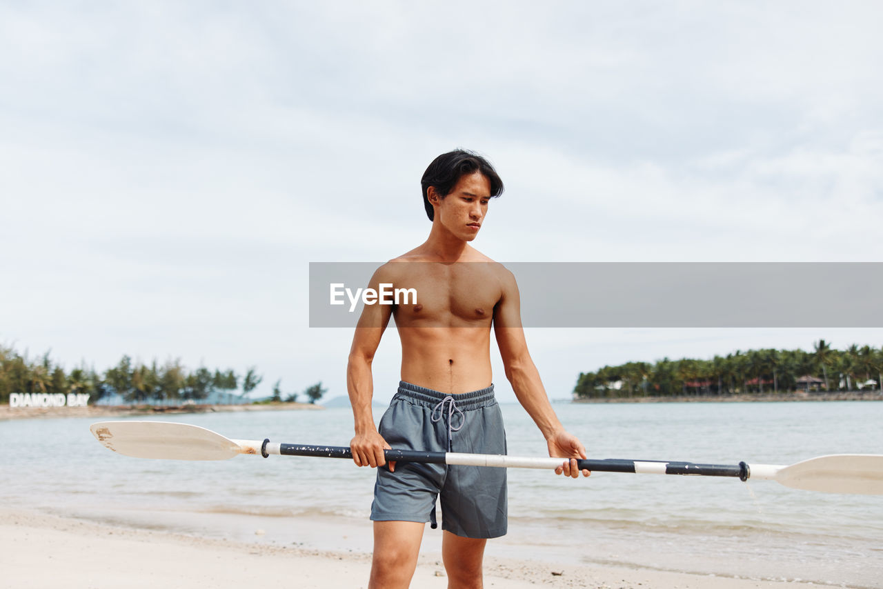 rear view of shirtless young man exercising at beach