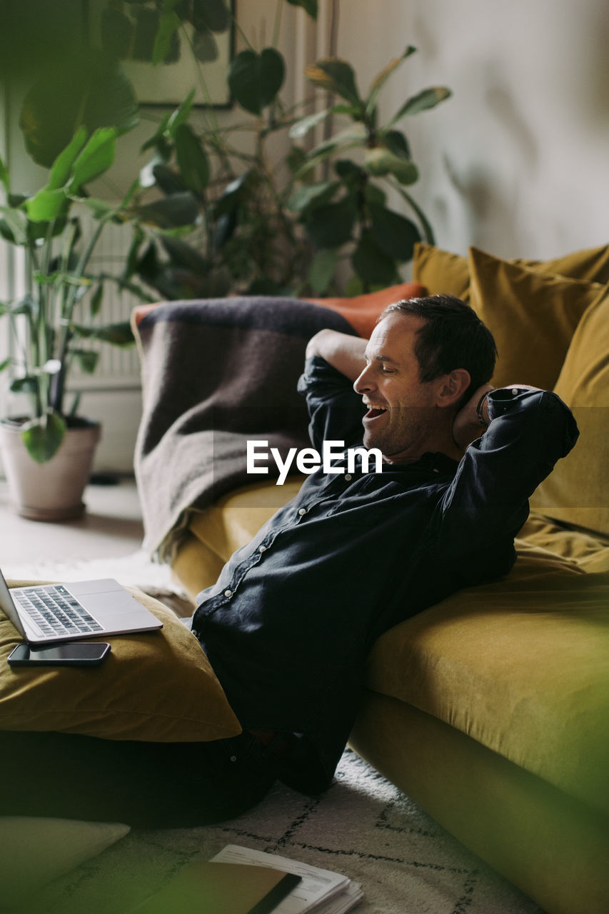 Male entrepreneur yawning with hands behind head in living room at home