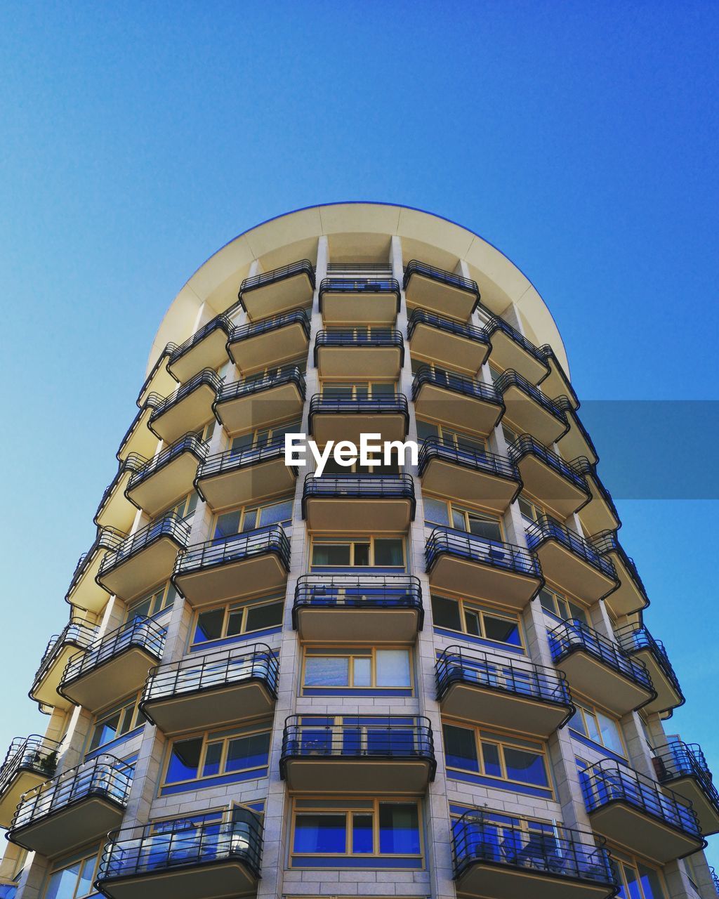 LOW ANGLE VIEW OF APARTMENT BUILDING AGAINST CLEAR BLUE SKY