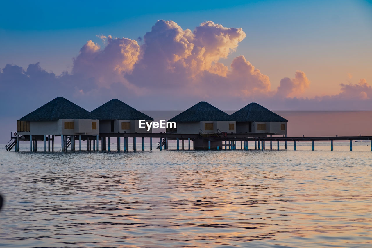 STILT HOUSE ON SEA BY BUILDINGS AGAINST SKY