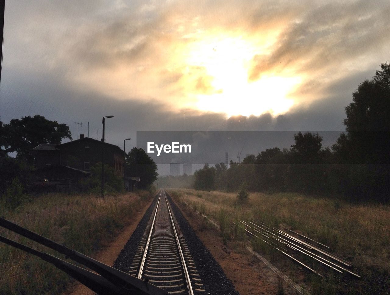 Railroad track amidst grassy field seen through windshield of locomotive against cloudy sky