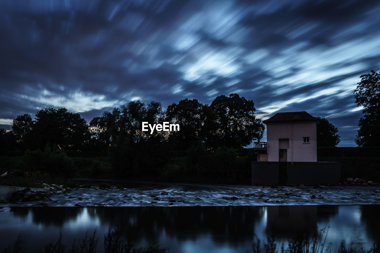 House by lake against cloudy sky at dusk