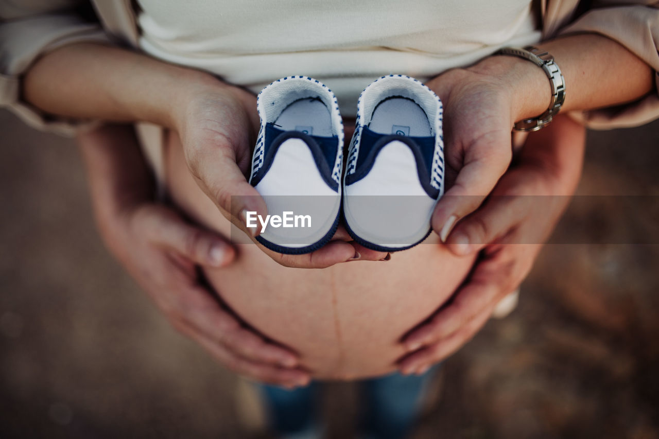 Low section of pregnant woman with man holding shoes while standing outdoors