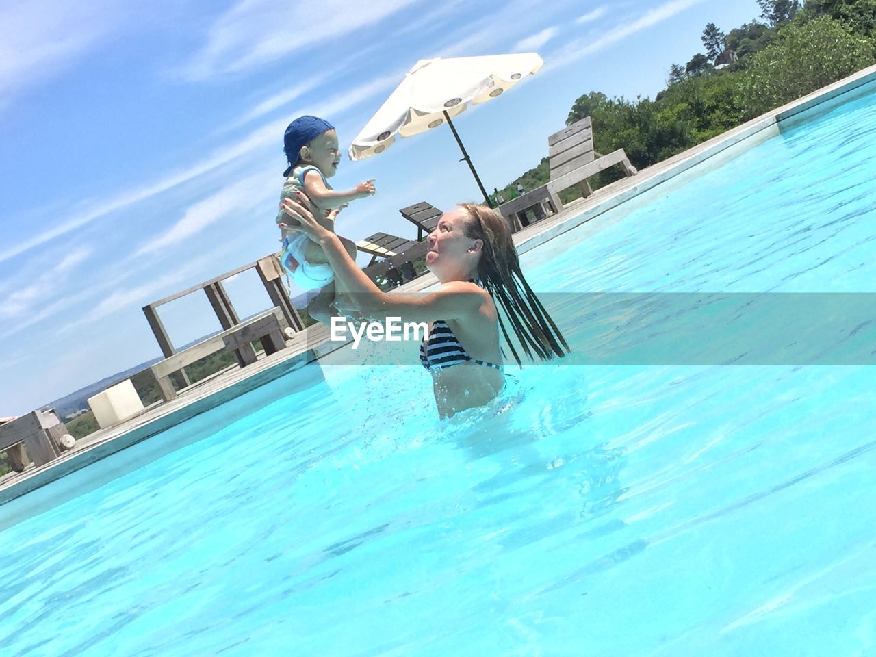 Tilted image of woman wearing bikini holding baby in swimming pool