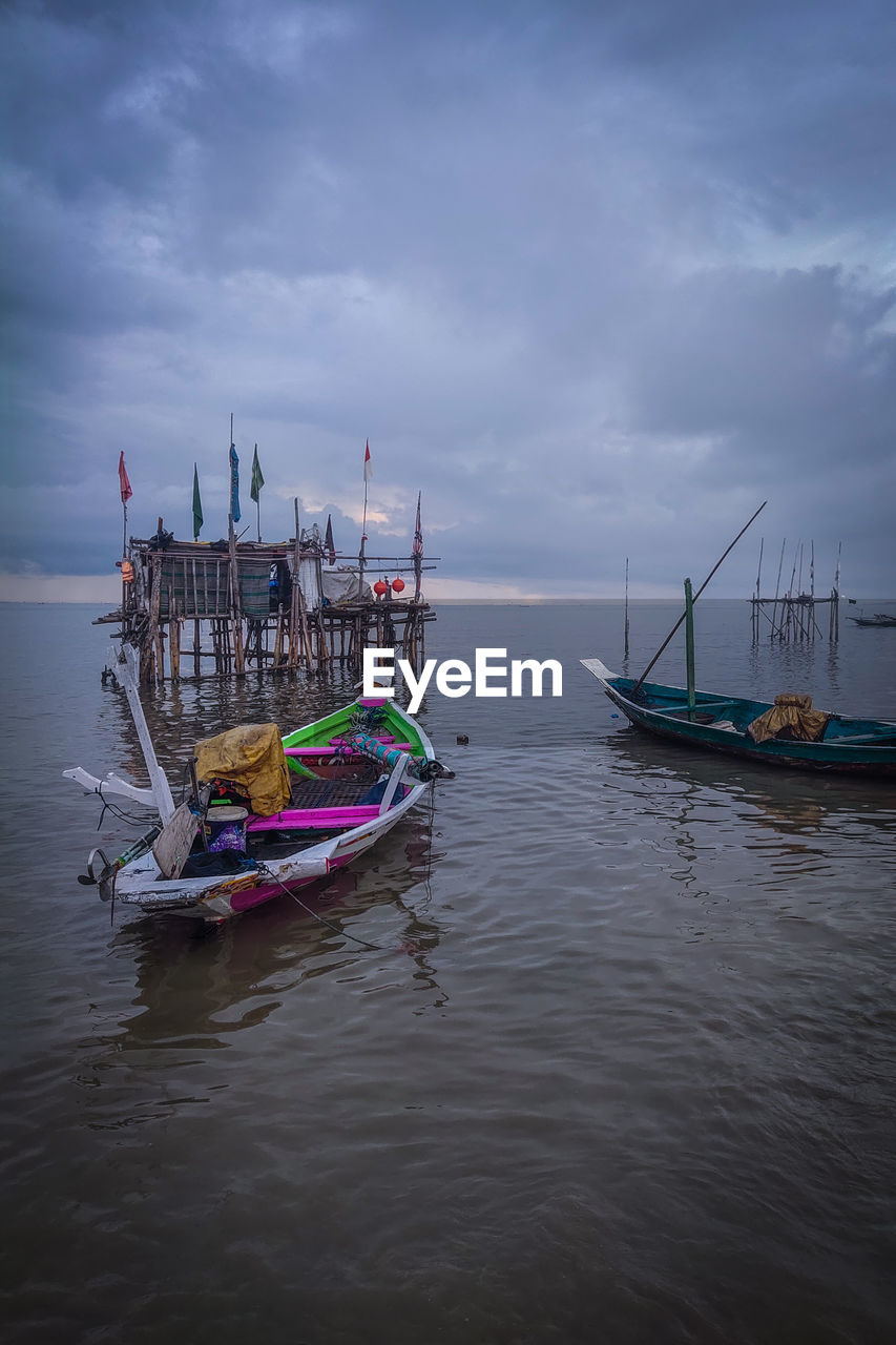 Fishing boats moored in sea against sky