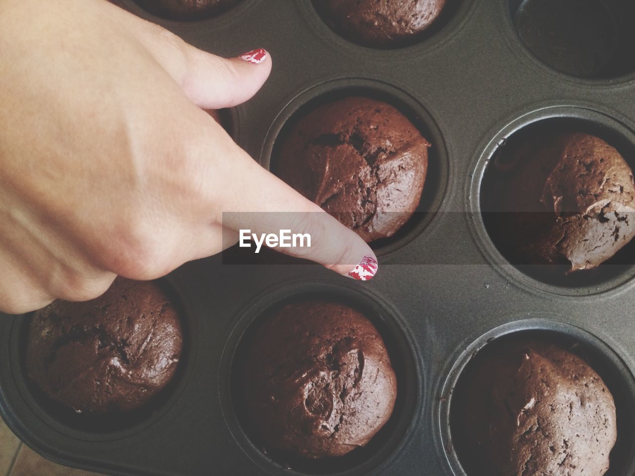 Cropped image of hand over brownie cupcakes in baking tray