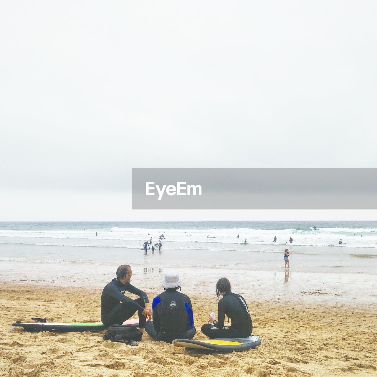 People with surfboards relaxing at beach against cloudy sky