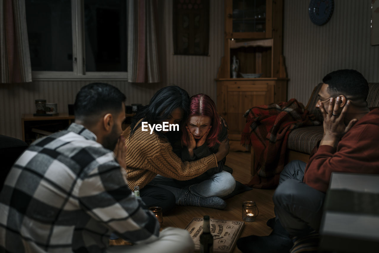 Terrified multiracial friends with ouija board in haunted cabin