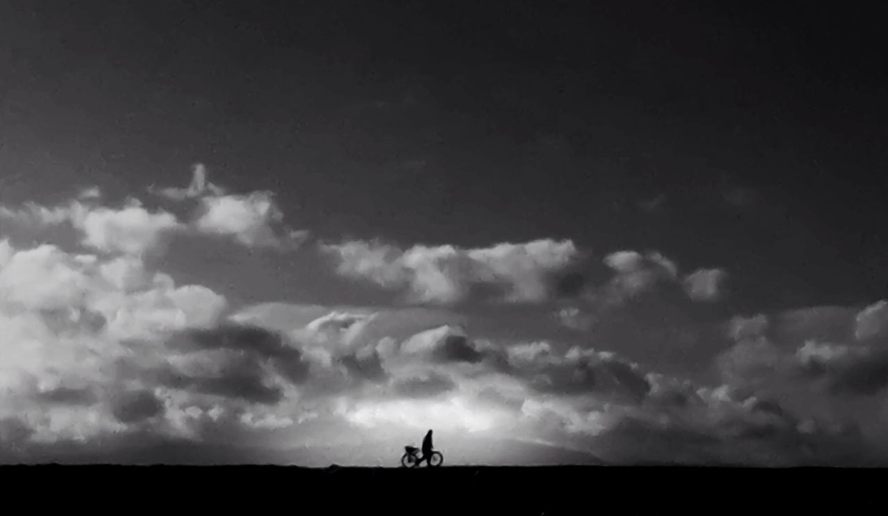 Scenic view of silhouette man walking bicycle against clouds in sky