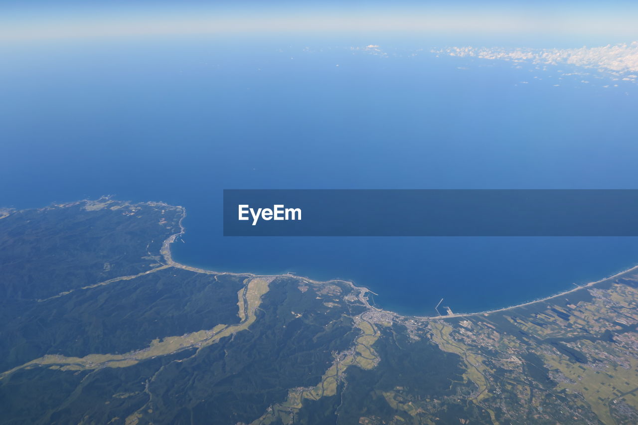 Aerial view of sea and mountains against blue sky